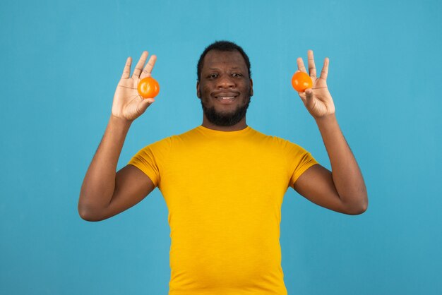 Ein lächelnder Afroamerikaner mit einer Mandarine in beiden Händen steht über der blauen Wand.