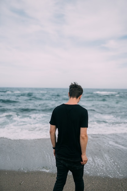 Ein lächelnder Mann in einem schwarzen T-Shirt steht an der sandigen Küste.