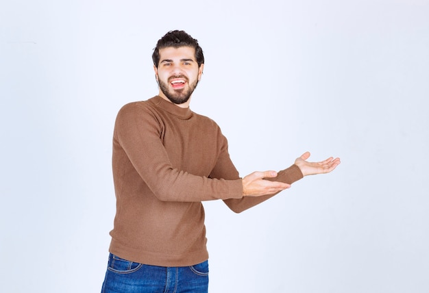 Ein lächelndes Modell des jungen Mannes, das Hände steht und zeigt. Foto in hoher Qualität