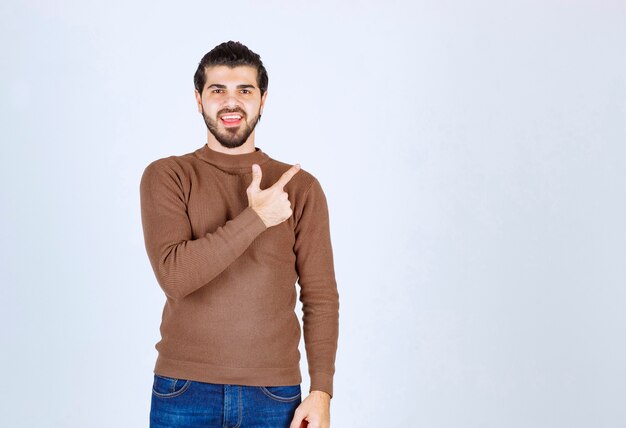 Ein lächelndes Modell des jungen Mannes, das mit einem Zeigefinger weg steht und zeigt. Foto in hoher Qualität