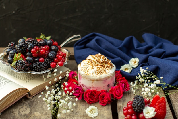 Ein leckeres Dessert aus der Nähe von oben um rote Rosen und frische Beeren auf dem braunen rustikalen Holzschreibtisch