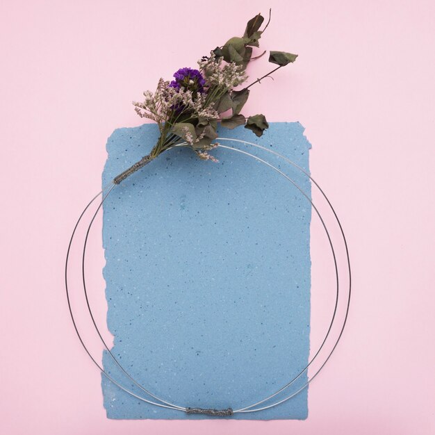 Ein leerer dekorativer Rahmen aus Metallkabel und Blumenstrauß auf Papier über rosa Hintergrund