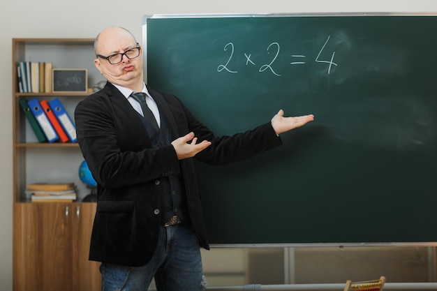 Kostenloses Foto ein lehrer mit brille steht neben der tafel im klassenzimmer und erklärt den unterricht und sieht enttäuscht aus