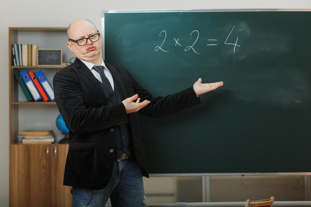 Ein Lehrer mit Brille steht neben der Tafel im Klassenzimmer und erklärt den Unterricht und sieht enttäuscht aus