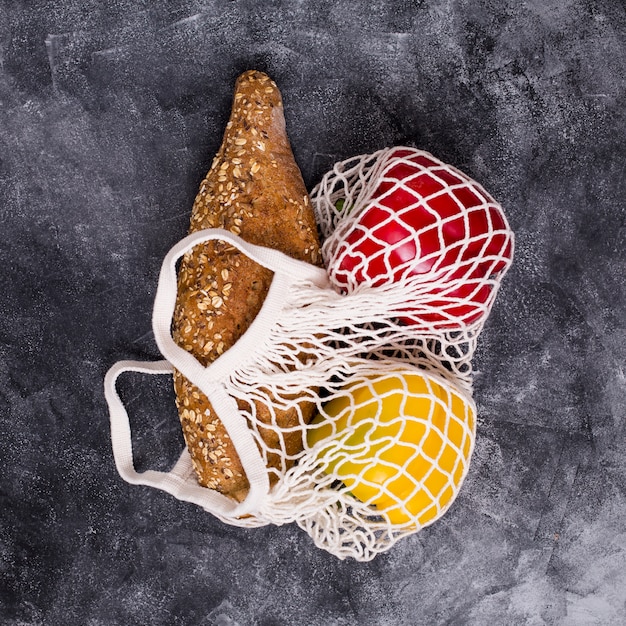 Ein Leib Brot; roter und gelber grüner Pfeffer in der weißen Netztasche auf strukturiertem Hintergrund