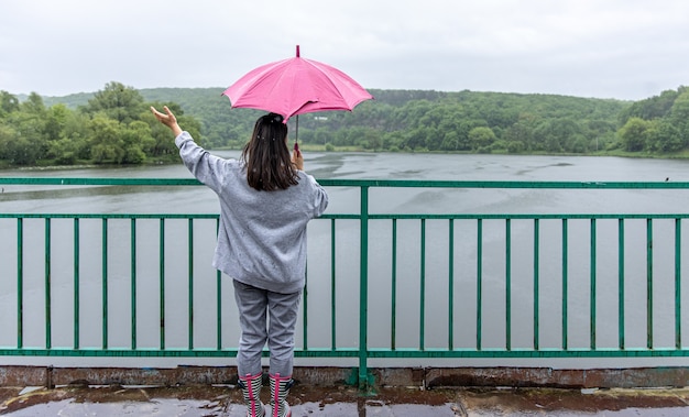 Ein Mädchen geht bei Regenwetter unter einem Regenschirm auf einer Brücke im Wald.