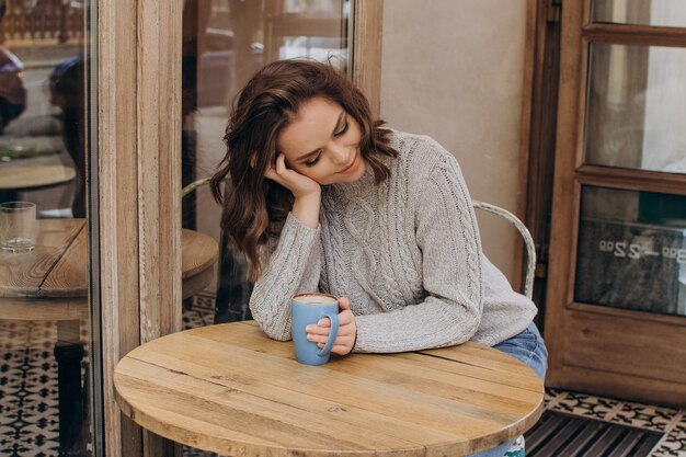 Ein mädchen in einem grauen pullover sitzt an einem tisch in einem café, trinkt kakao und lächelt