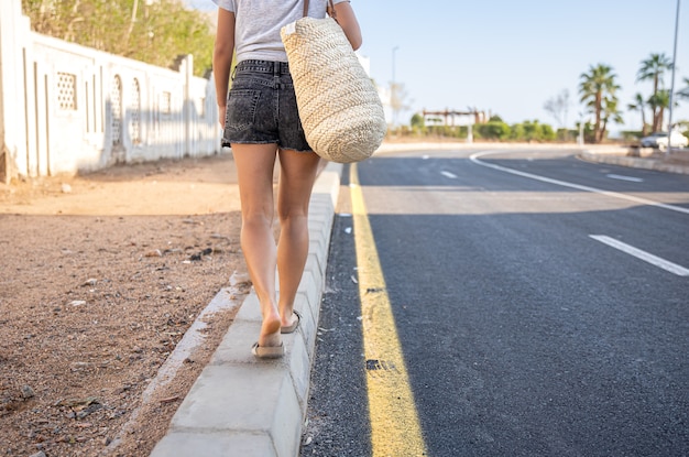 Ein Mädchen mit gebräunten Beinen geht den Bürgersteig entlang der Straße mit Tasche.