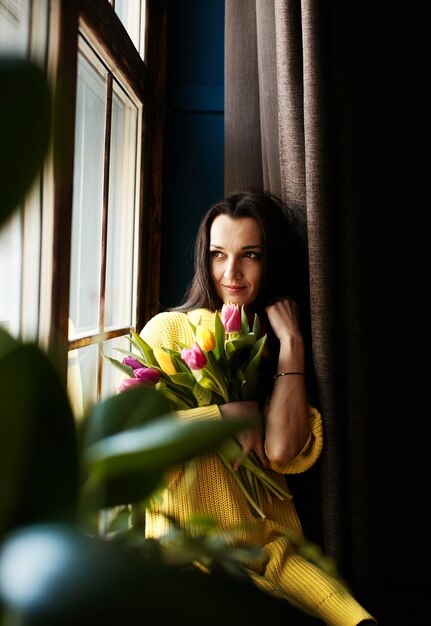 Ein Mädchen mit Tulpen schaut aus dem Fenster