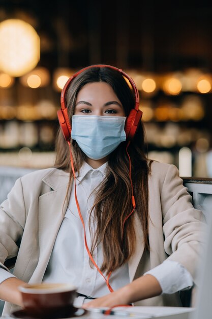 Ein Mädchen sitzt in einem Café mit Kopfhörer Coronavirus Ausbruch