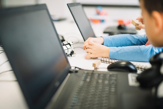 Ein Mädchenkind, das mit hölzernem Würfelpuzzlespiel mit Laptop auf weißem Schreibtisch spielt