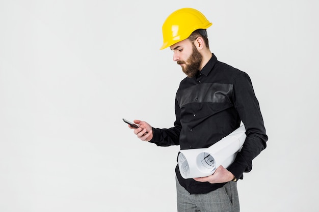 Ein männlicher Architekt, der den gelben Hardhat betrachtet Smartphone trägt