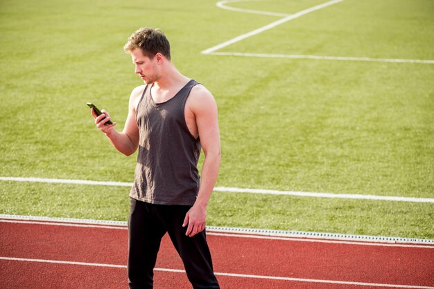 Ein männlicher Athlet, der auf Stadion unter Verwendung des Handys steht