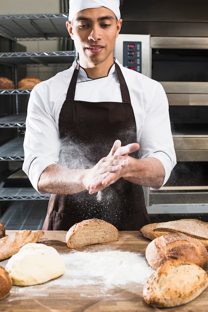 Ein männlicher Bäcker, der das Mehl mit den Händen auf geknetetem Teig abwischt