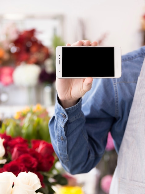 Ein männlicher Florist, der Bildschirm des Handys im Blumenladen zeigt