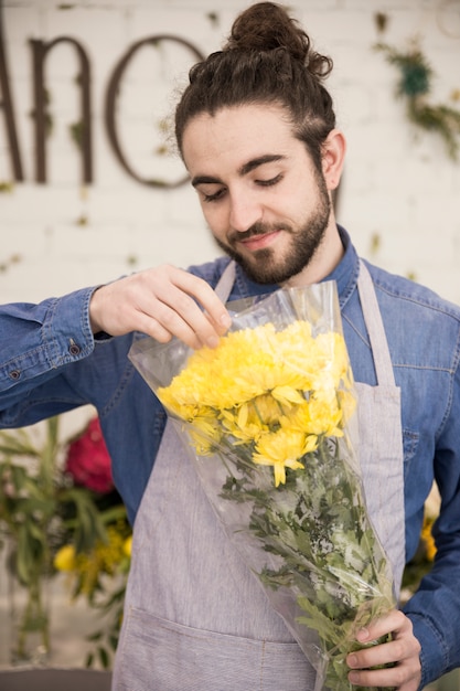 Ein männlicher Florist, der die gelbe Chrysantheme einwickelt, blüht in das Plastikpapier
