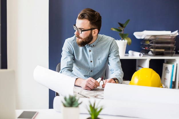 Ein männlicher Ingenieur, der am Arbeitsplatz mit Architekturplan auf Tabelle sitzt