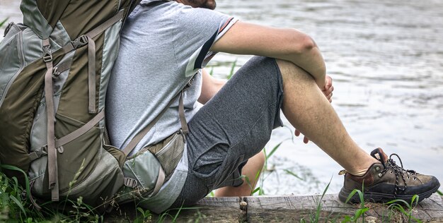 Ein männlicher Reisender mit einem großen Wanderrucksack ruht sich in der Nähe des Flusses aus.