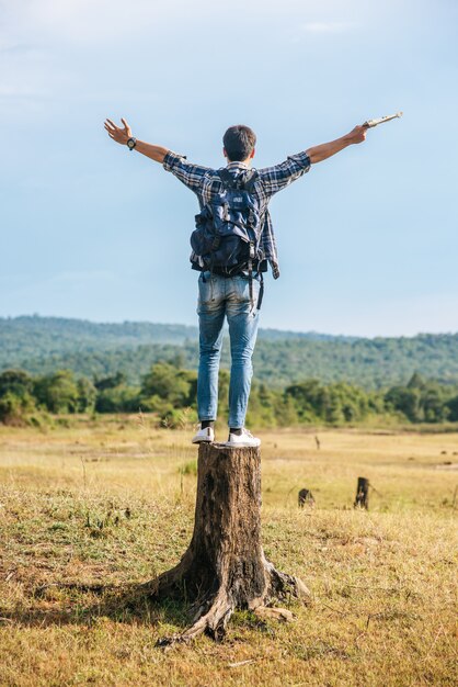 Ein männlicher Reisender mit einem Rucksack, der eine Karte trägt und auf einem Baumstumpf steht