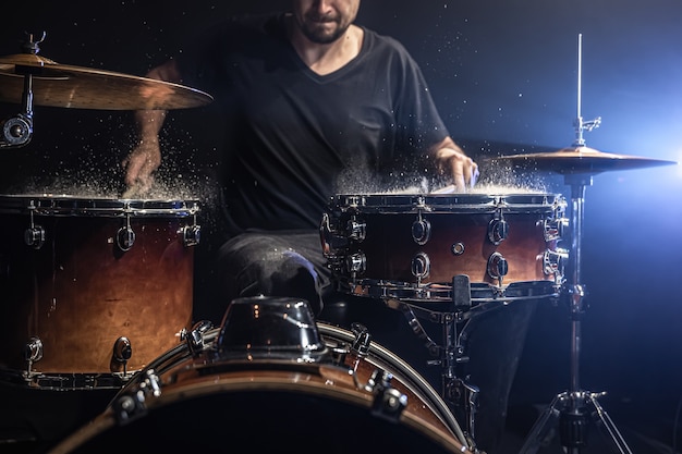 Ein männlicher Schlagzeuger spielt Trommelstöcke auf einer Snare-Drum mit Spritzwasser in einem dunklen Raum.