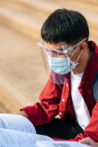 Ein männlicher Student, der eine Maske trägt und beim Lesen sitzt.