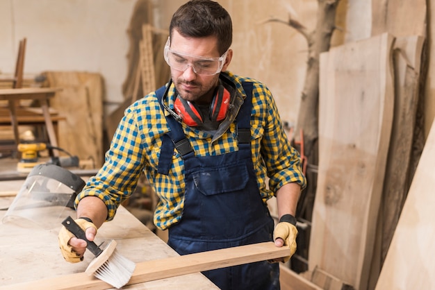 Ein männlicher Tischler, der die hölzerne Planke mit Bürste in der Werkstatt säubert