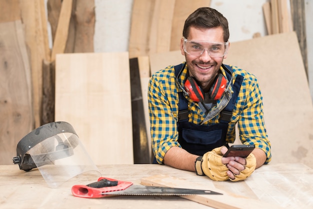 Kostenloses Foto ein männlicher tischler, der hinter dem werktisch unter verwendung des handys steht