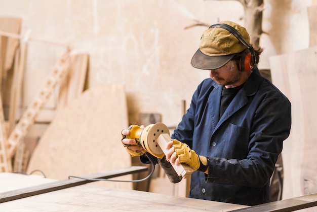 Kostenloses Foto ein männlicher tischler, der mit schwingschleifer für die formung des holzblocks arbeitet