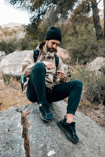 Ein männlicher Wanderer, der auf dem Felsen betrachtet Navigationskompaß sitzt