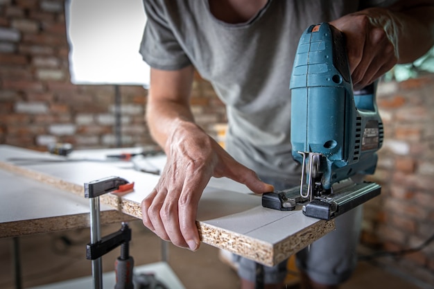 Ein männlicher Zimmermann schneidet ein Holz mit einer elektrischen Stichsäge und arbeitet mit einem Baum.