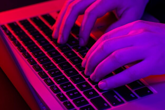 Ein Mann benutzt einen Laptop, Nahaufnahme, männliche Hände in Neonbeleuchtung