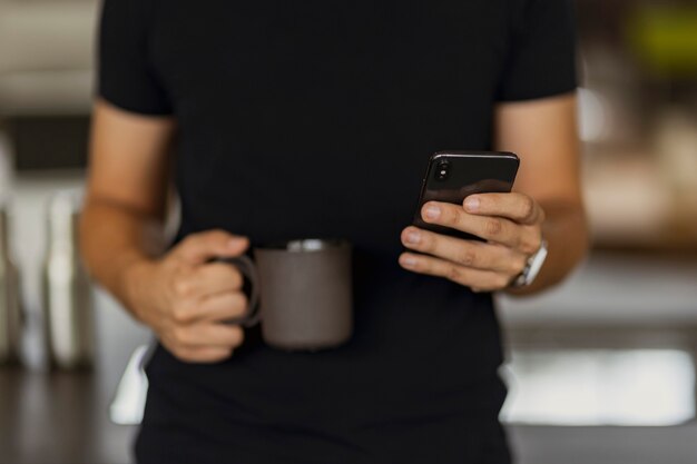 Ein Mann, der auf seinem Handy eine SMS schreibt, während er eine schwarze Kaffeetasse in der anderen Hand hält