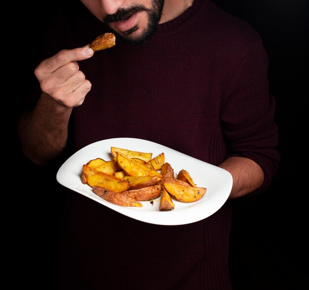 Ein Mann, der Bratkartoffeln von der weißen Platte schmeckt