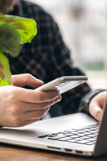 Ein Mann hält ein Smartphone und arbeitet an einem Laptop