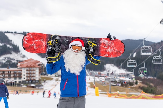 Ein mann in einer weihnachtsmütze mit einem snowboard in einem skigebiet. Premium Fotos