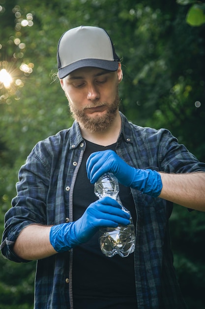 Ein mann in handschuhen mit einer plastikflasche in den händen reinigt den wald