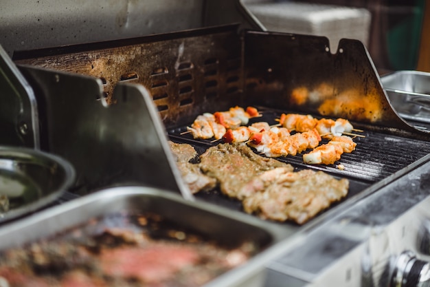 Ein Mann in Tätowierungen macht Barbecue Grill Fleisch im Freien.