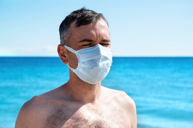 Ein Mann in weißer medizinischer Maske am Meer