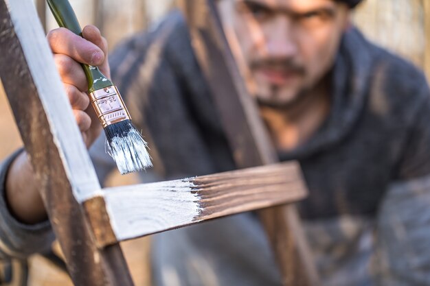 Ein Mann malt mit weißer Farbe auf Holzbrettern. Mann im industriellen Konzept. Es gibt einen Platz für Text, das Objekt ist nah