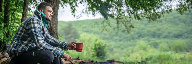 Ein Mann mit einem Becher wärmenden Getränks wärmt sich am Feuer im Wald