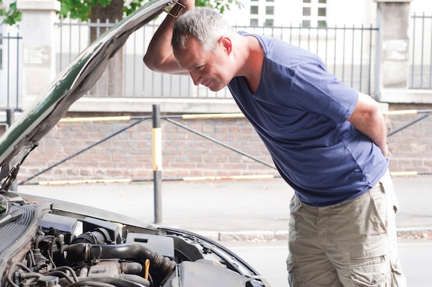 Ein Mann mit einem schlechten Tag überprüft unter der Motorhaube seines Autos zu figu