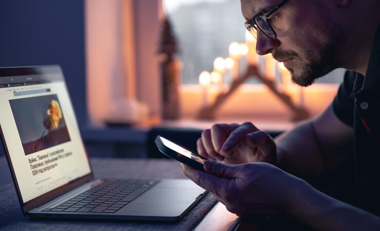 Kostenlose Foto ein mann mit einem smartphone sitzt spät abends vor einem laptop