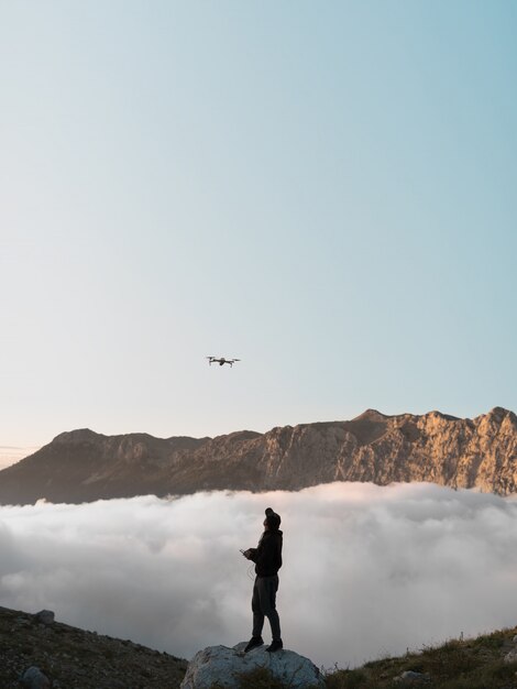 Ein Mann mit einer Drohne in den Bergen fliegt hinter den Wolken