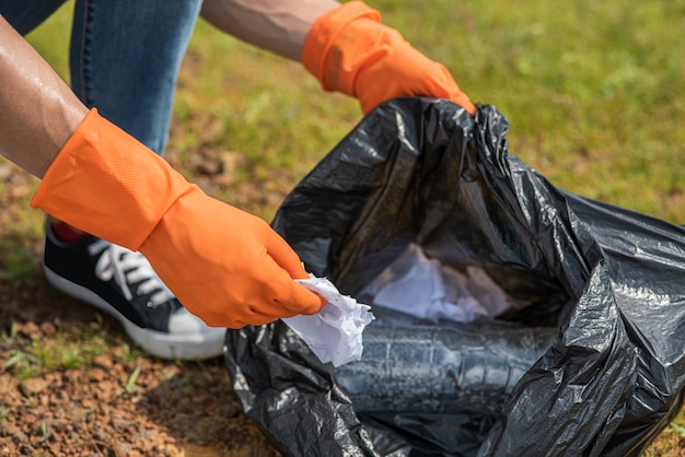 Ein Mann mit orangefarbenen Handschuhen sammelt Müll in einer schwarzen Tasche.