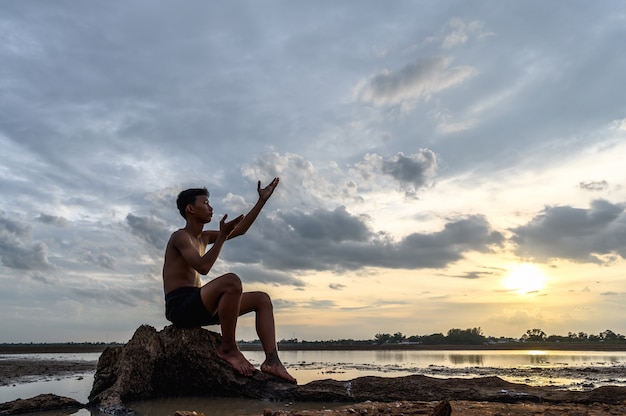 Ein Mann saß mit gebeugten Knien, machte ein Handsymbol, um am Baumstamm nach Regen zu fragen, und war von Wasser umgeben.