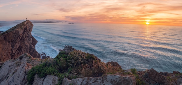 Ein Mann schaut bei Sonnenuntergang von einer Klippe auf das Meer.