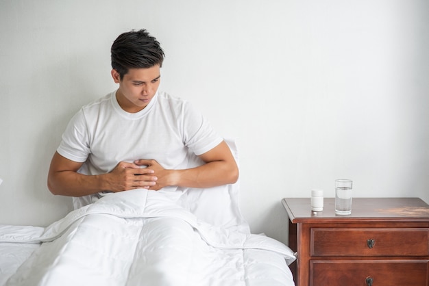 Ein mann sitzt mit bauchschmerzen im bett und drückt sich mit den händen auf den bauch.