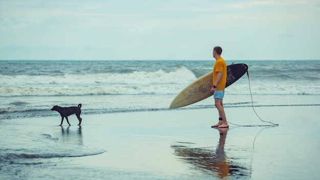 Ein Mann steht mit einem Surfbrett am Strand.