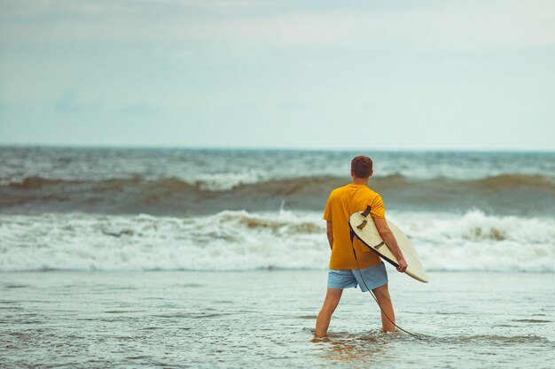 Ein Mann steht mit einem Surfbrett am Strand.