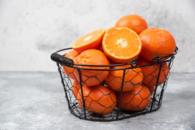 Ein metallischer schwarzer Korb voller saftiger Orangenfrüchte auf Steintisch.